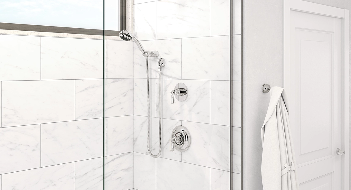 Modern bathroom with a white marble tiled shower and bathtub. Chrome fixtures, clear glass door, wall hook with a white robe, and window create a fresh, clean feel.